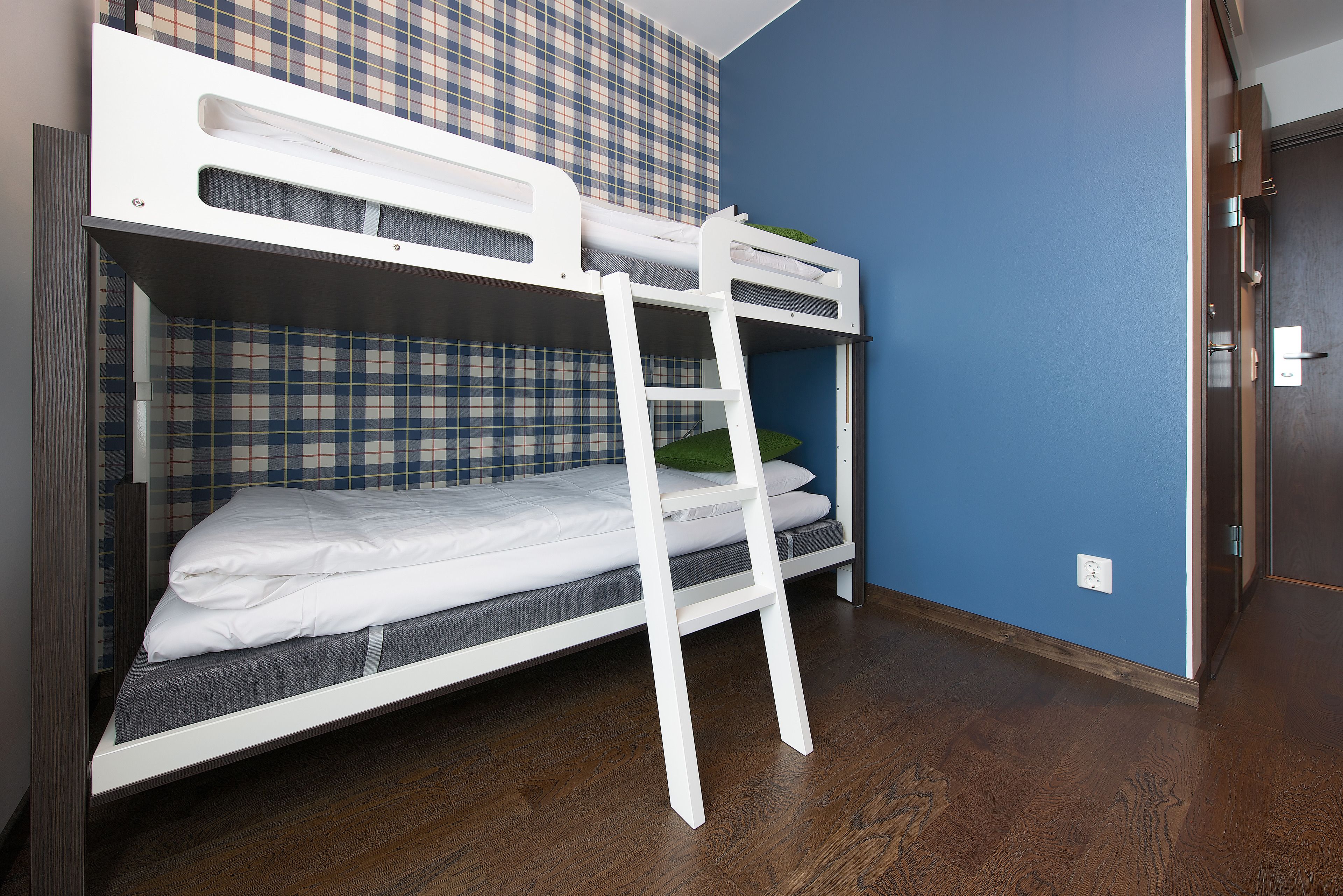 Una cama litera con escalera, pared con estampado escocés y suelo de madera.