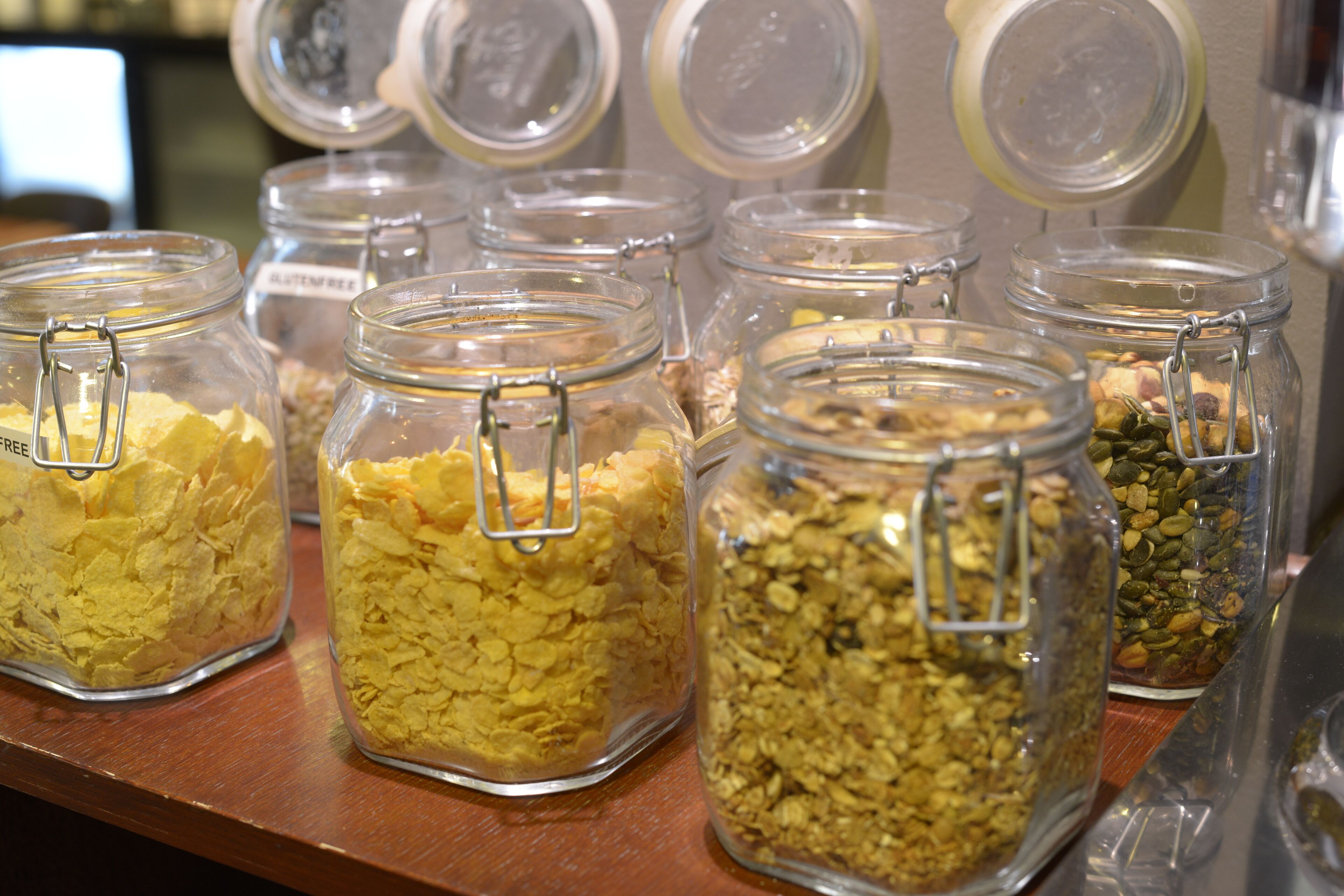 Frascos de vidrio con cierres metálicos que contienen diversos alimentos sobre un estante de madera.