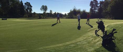 A golf course with players and a golf cart.