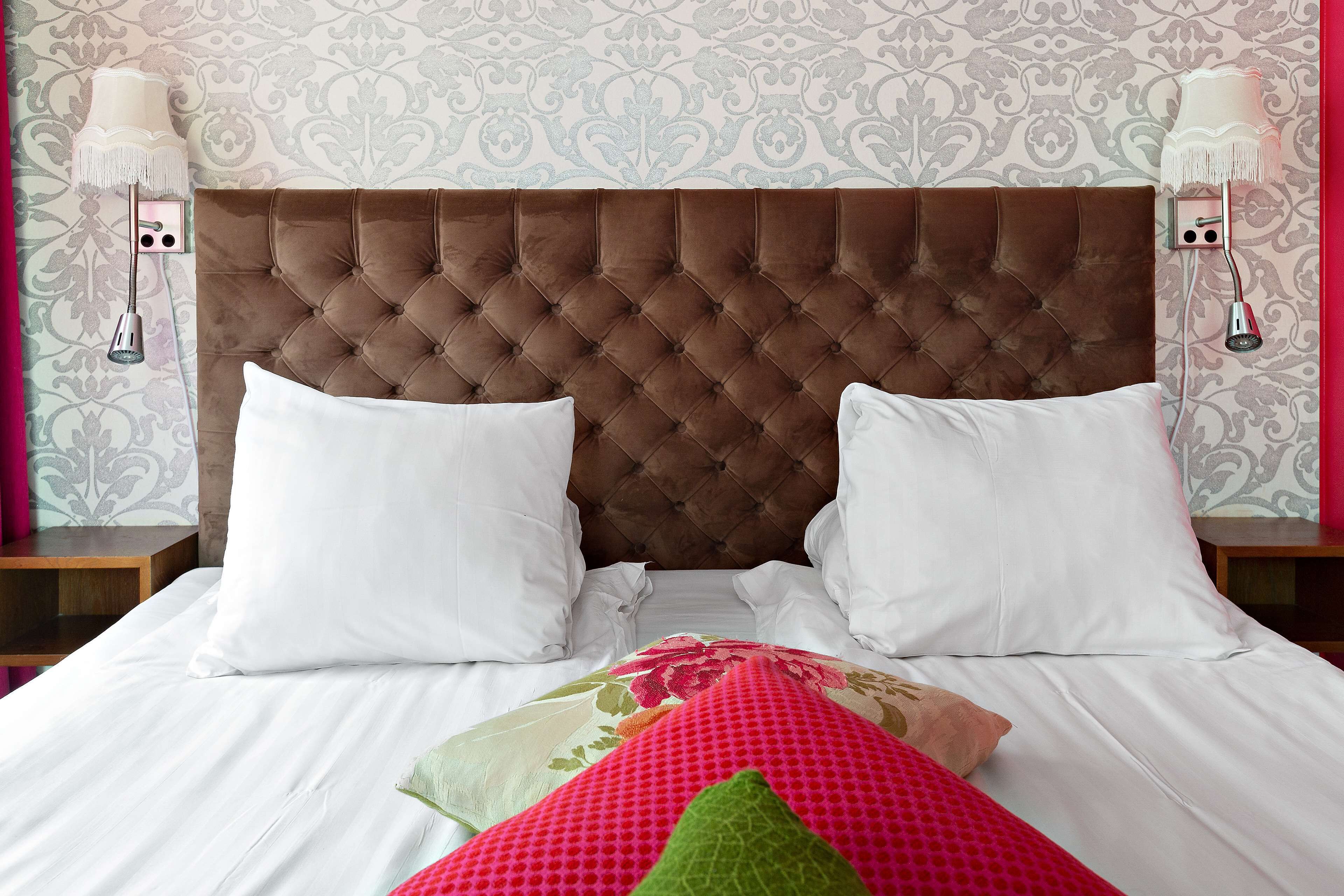 Un lit bien fait, avec une tête de lit capitonnée, des oreillers blancs et une couvre-lit à motifs floraux.