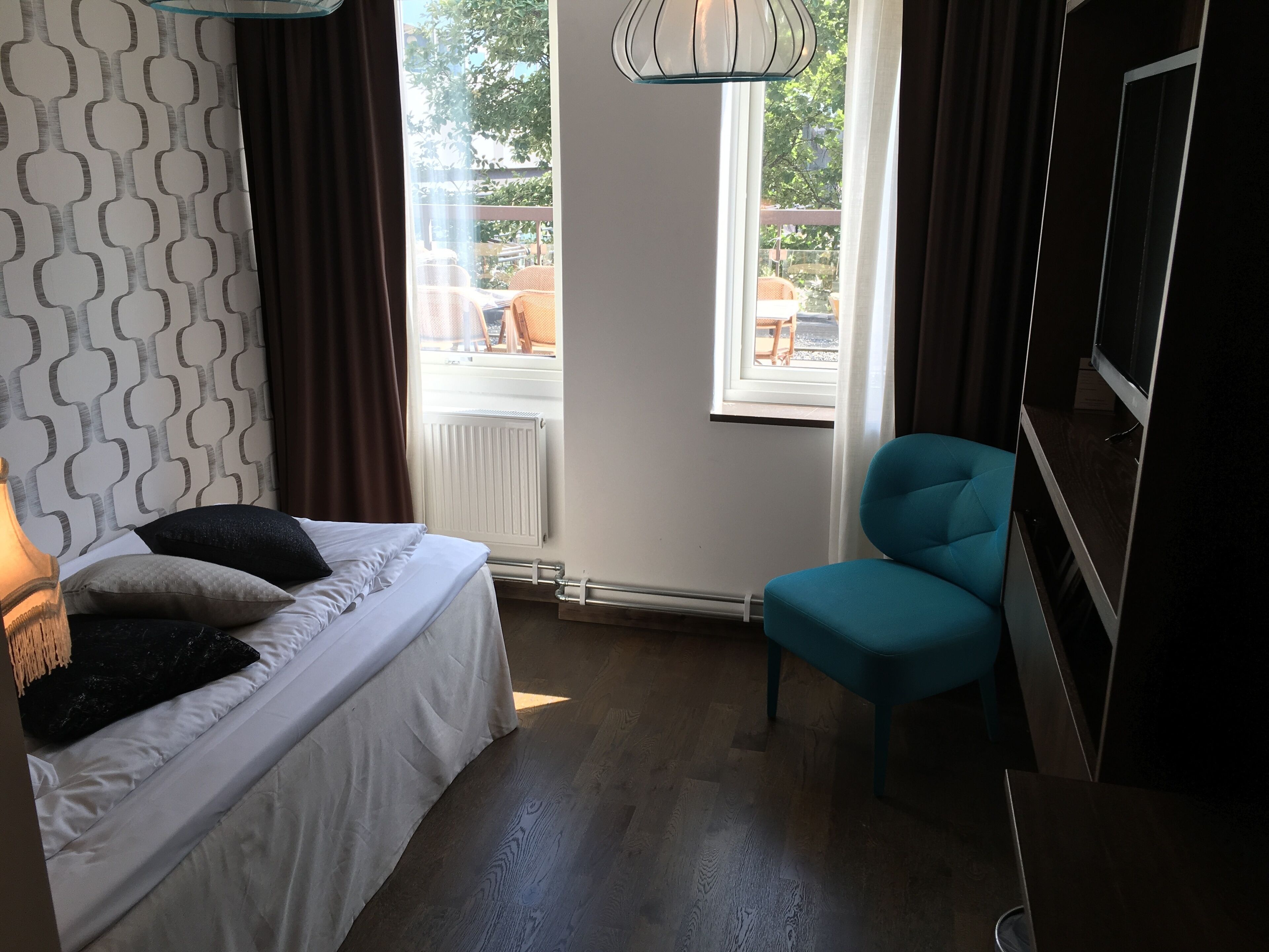 A bedroom with a bed, a blue chair, a TV, and a window with a view of the outdoors.