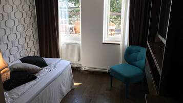 A bedroom with a bed, a blue chair, a TV, and a window with a view of the outdoors.