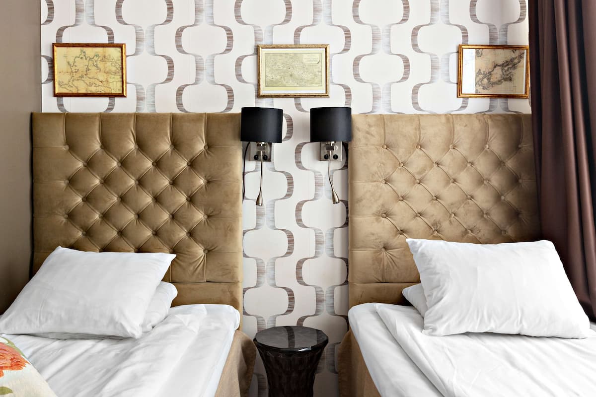 A hotel room with a tufted headboard, two beds with white linens, a small round table, and wall-mounted lamps.