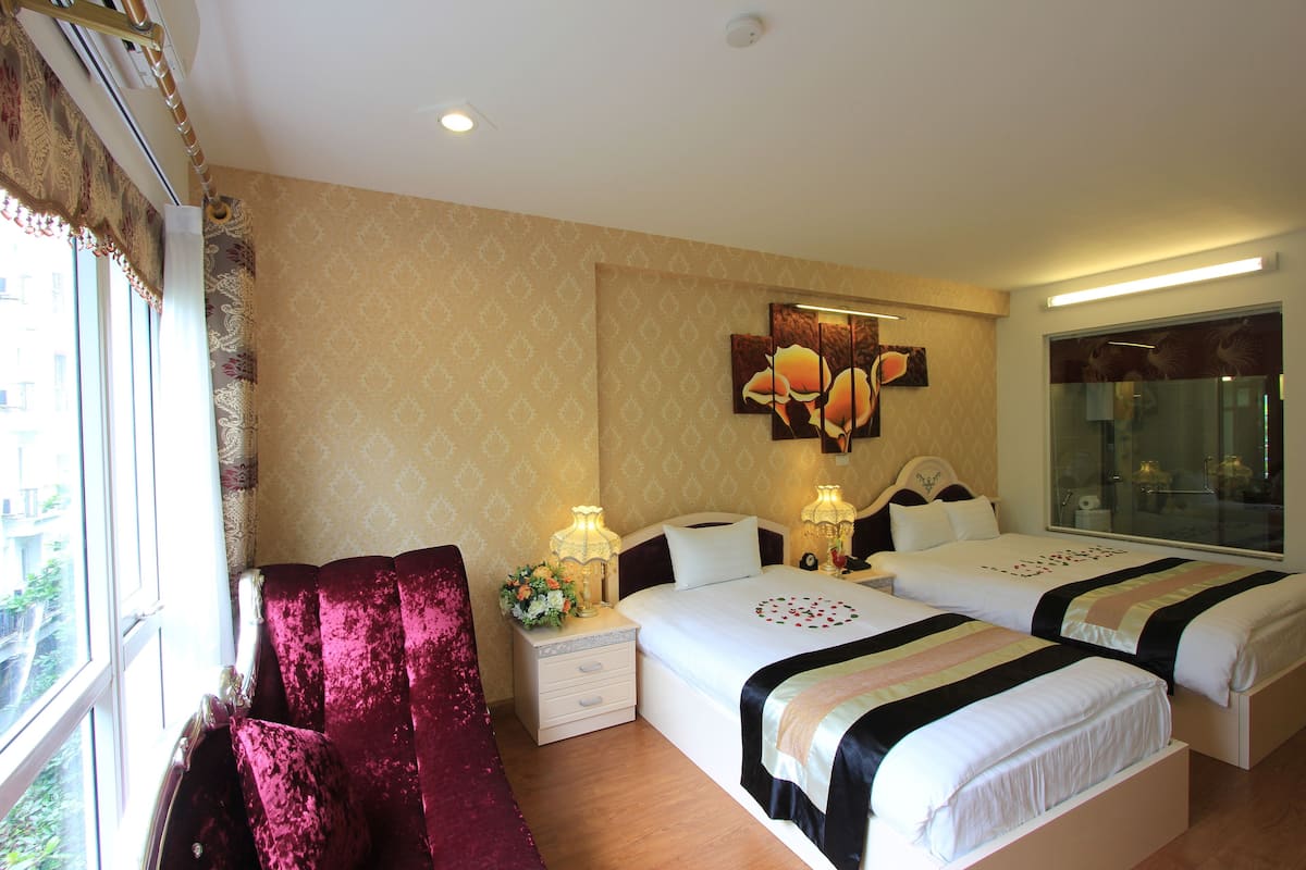 A hotel room with two beds, a large window, a decorative wall piece, and a nightstand with lamps.