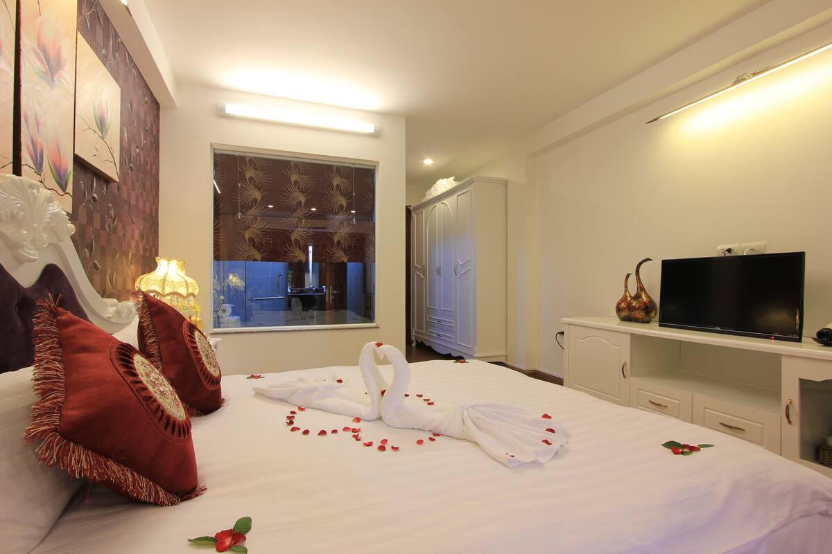 A hotel room with a bed, pillows, a TV, and a wardrobe.
