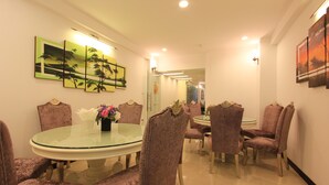A dining area with a round glass table surrounded by velvet chairs, framed artwork on the walls, and a mirror reflecting the room.