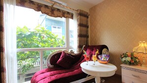 A room with a large window, a plush red sofa, a small round table with drinks, and a decorative lamp.