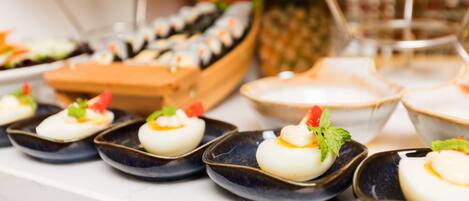 Un bufé con diversos platos, incluyendo sushi, huevos rellenos y una piña.