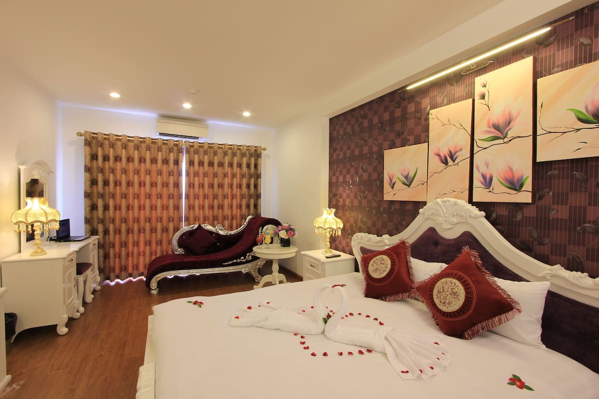 A hotel room with a large bed, a desk, a vanity, and a chair.