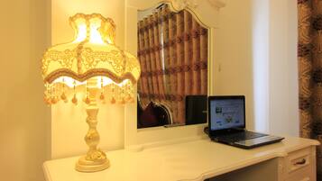 Ett vitt skrivbord med en bärbar dator, en dekorativ lampa och en spegel som reflekterar gardinerna.