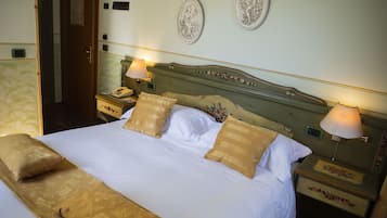 Una cama bien hecha con sábanas blancas y dos almohadas decorativas, flanqueada por mesitas de noche con lámparas y un reloj.
