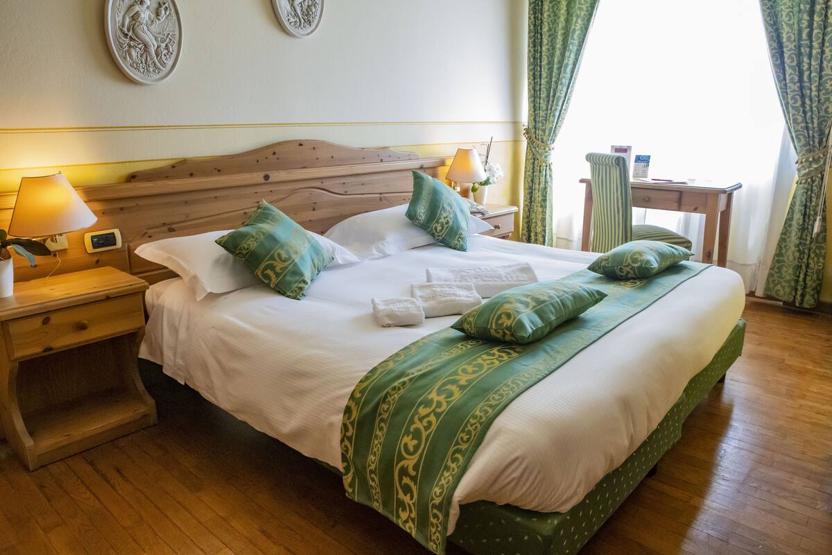 A neatly made bed with green and white bedding, a wooden headboard, and a bedside table with a lamp and a clock.