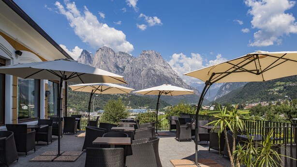 An outdoor patio with wicker furniture and large umbrellas, overlooking a mountainous landscape. - Villa Imperina (Agordo)
