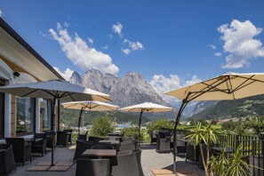 An outdoor patio with wicker furniture and large umbrellas, overlooking a mountainous landscape. - Villa Imperina (Agordo)