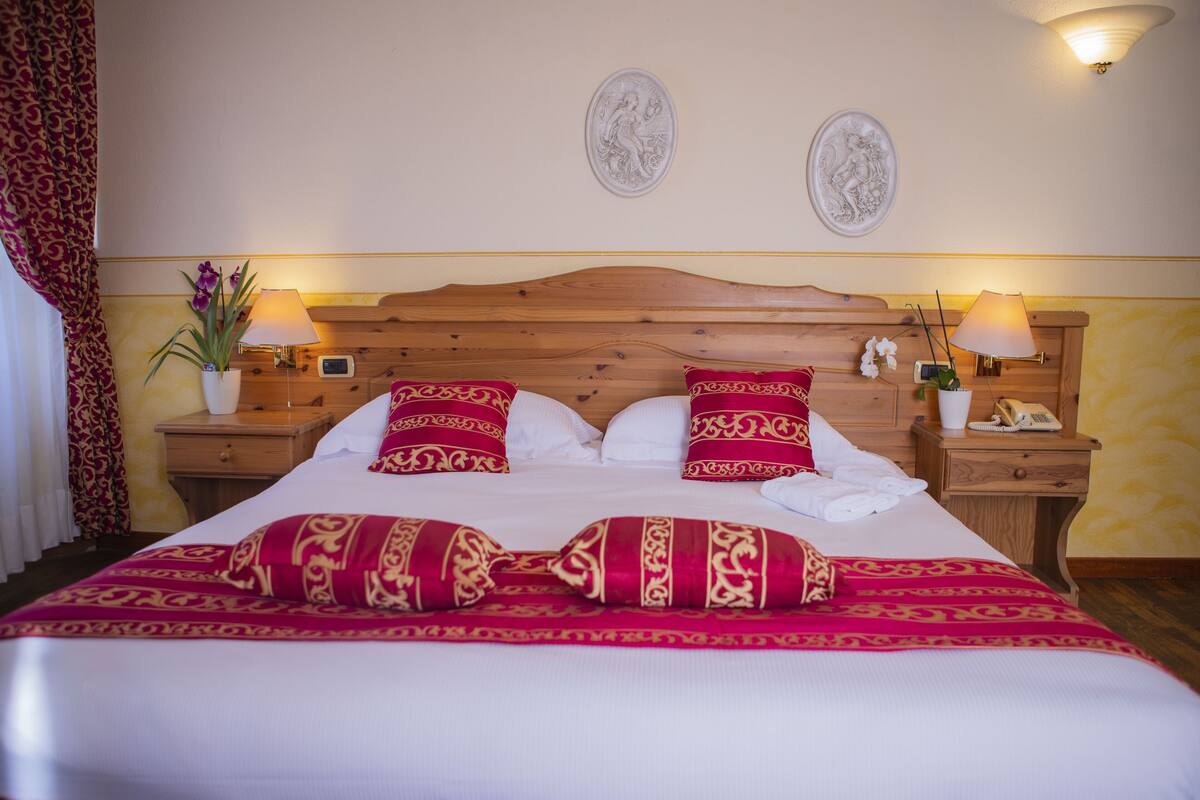 A neatly made bed with red and white bedding, two wall-mounted sconces, and a wooden headboard.