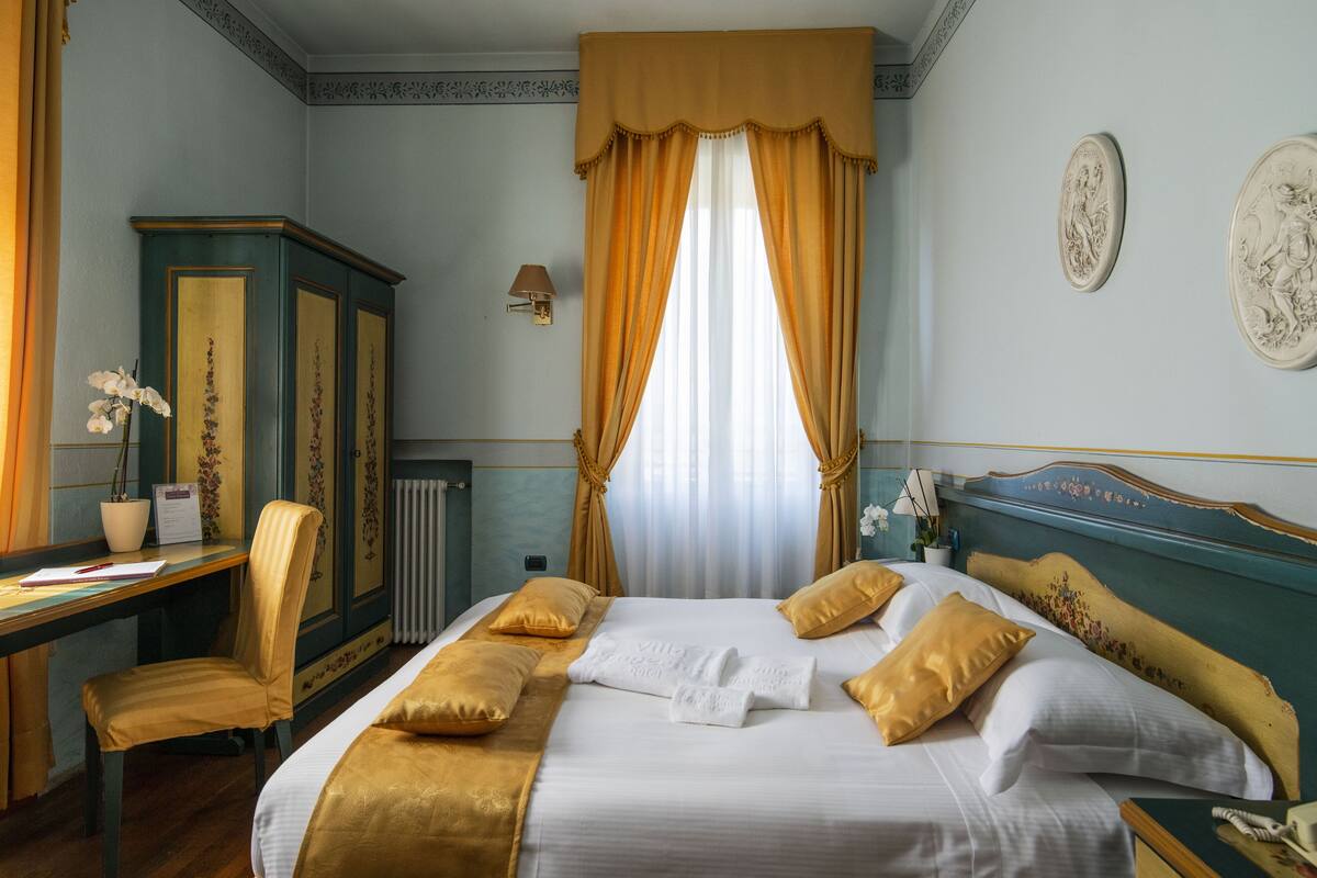 A hotel room with a bed, a desk, a chair, and a radiator.