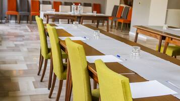 A conference room with long tables, green chairs, and white tablecloths.
