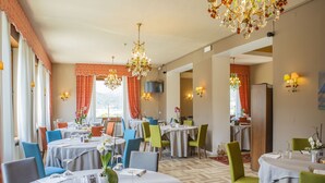 A dining area with round tables, chairs, chandeliers, and wall-mounted lights. - Villa Imperina (Agordo)