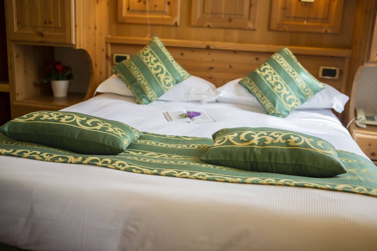 A neatly made bed with green and white patterned pillows, a small potted plant, and a wooden headboard.