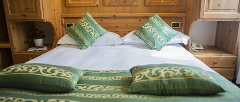 Una habitación con paneles de madera, una cama, dos lámparas de noche, un mesita de noche y una pequeña mesa con una planta en maceta.