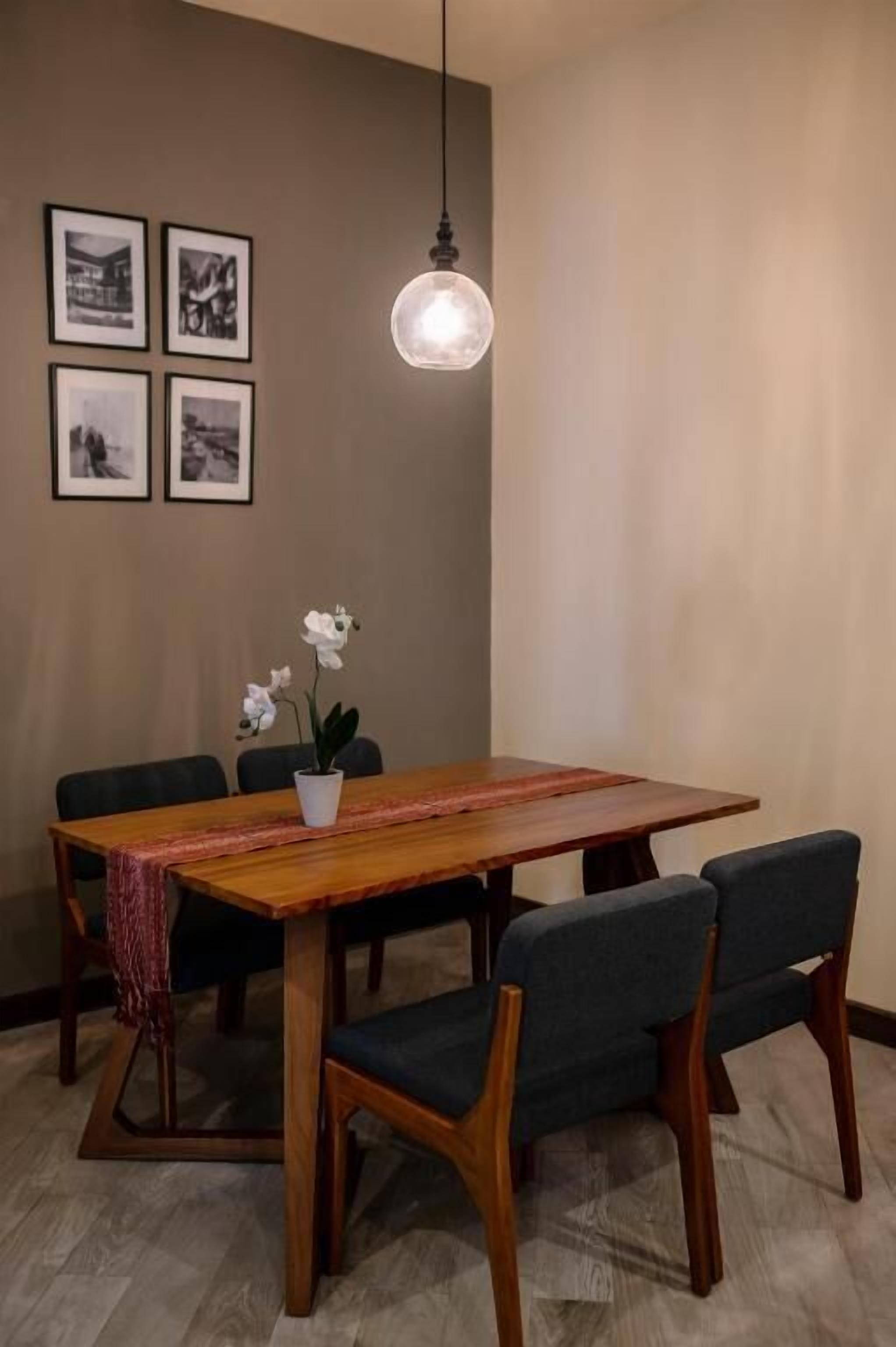Un comedor con mesa y sillas de madera, una lámpara colgante y cuadros en la pared.