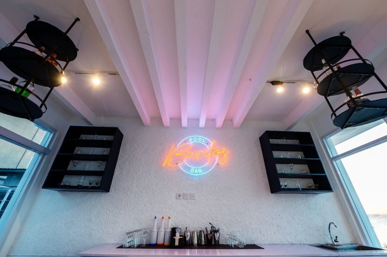 A bar area with a neon sign reading "Pool Bar," shelves with glasses, and a modern ceiling design.