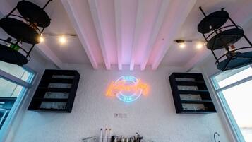 A bar area with a neon sign reading "Pool Bar," shelves with glasses, and a modern ceiling design.
