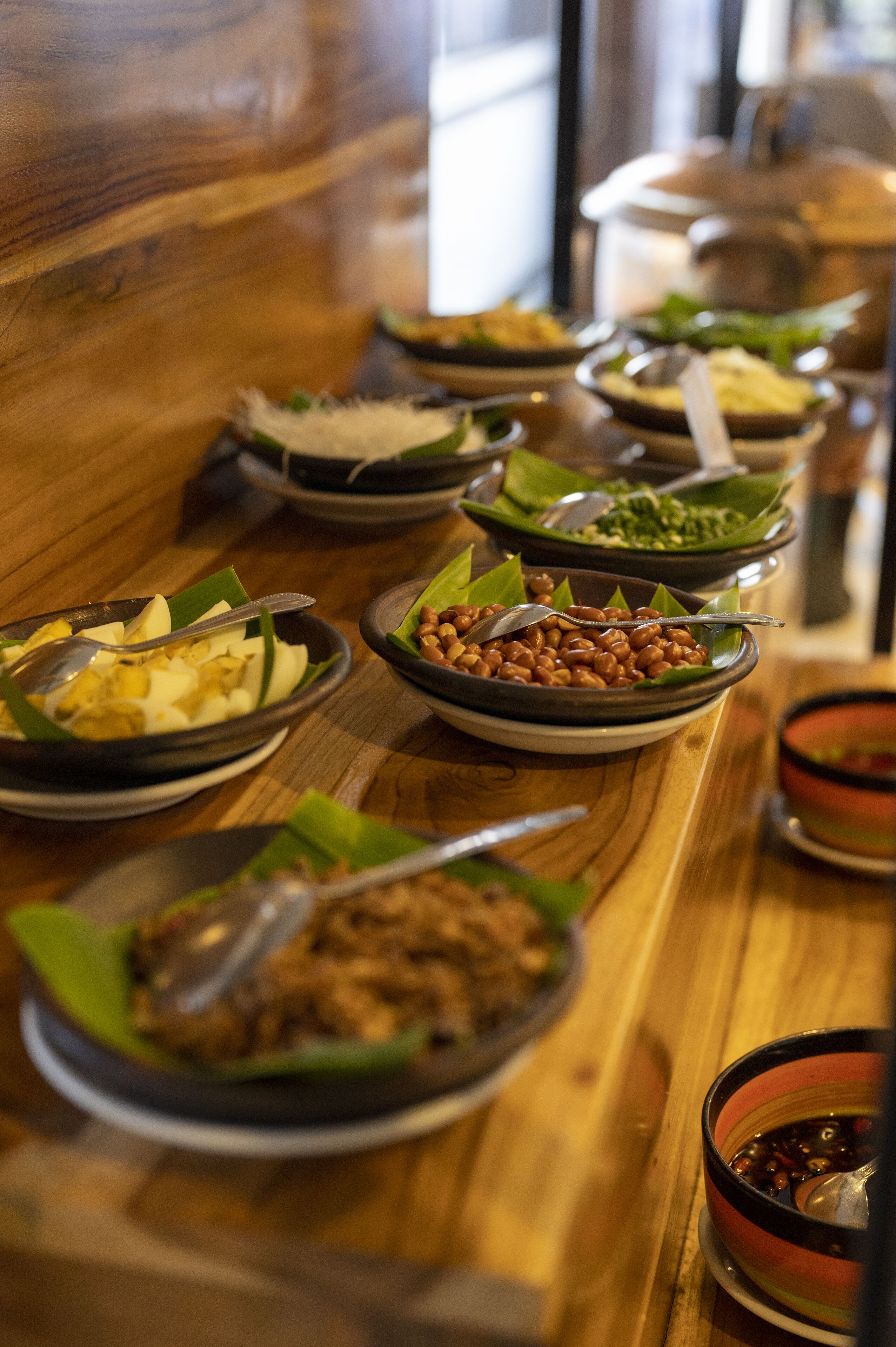 A buffet table with various dishes, including a bowl of peanuts, a bowl of vegetables, and a bowl of soup.
