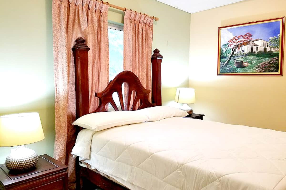 Un dormitorio con una cama de madera, dos mesitas de noche con lámparas, una ventana con cortinas y un cuadro en la pared.