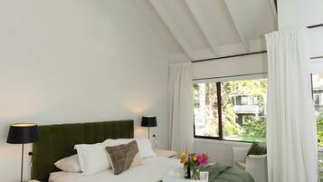 A bedroom with a green bed, white walls, a window with curtains, and a nightstand with a lamp.