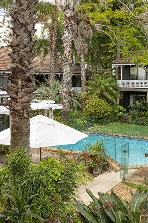 A pool area with palm trees, a white umbrella, and a brick pool.