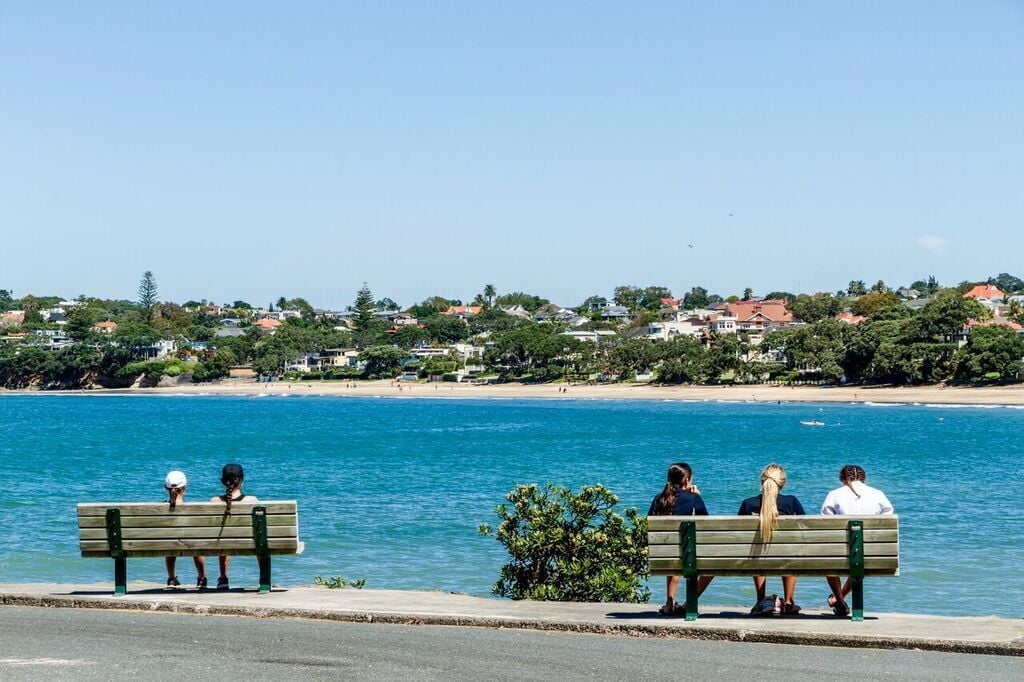 Une vue sur la côte, avec un banc donnant sur la mer, un ciel dégagé et une zone résidentielle en arrière-plan.