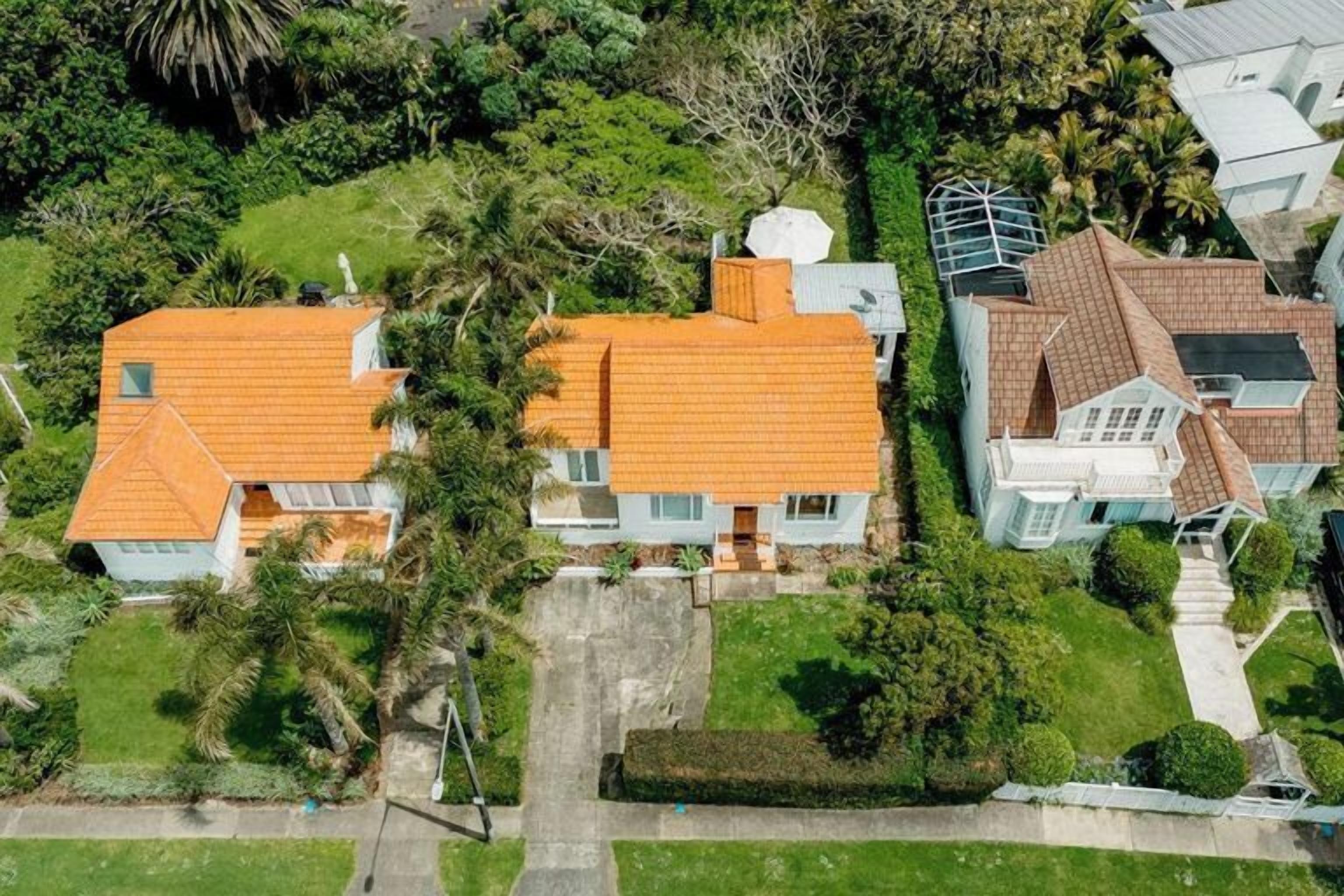 Ett flygbildsbild av ett bostadsområde med två hus, båda med röda tegeltak, omgivna av frodig grönska och palmer.