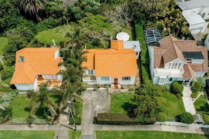 An aerial view of a residential area with two houses, each with a red-tiled roof, surrounded by lush greenery and palm trees.