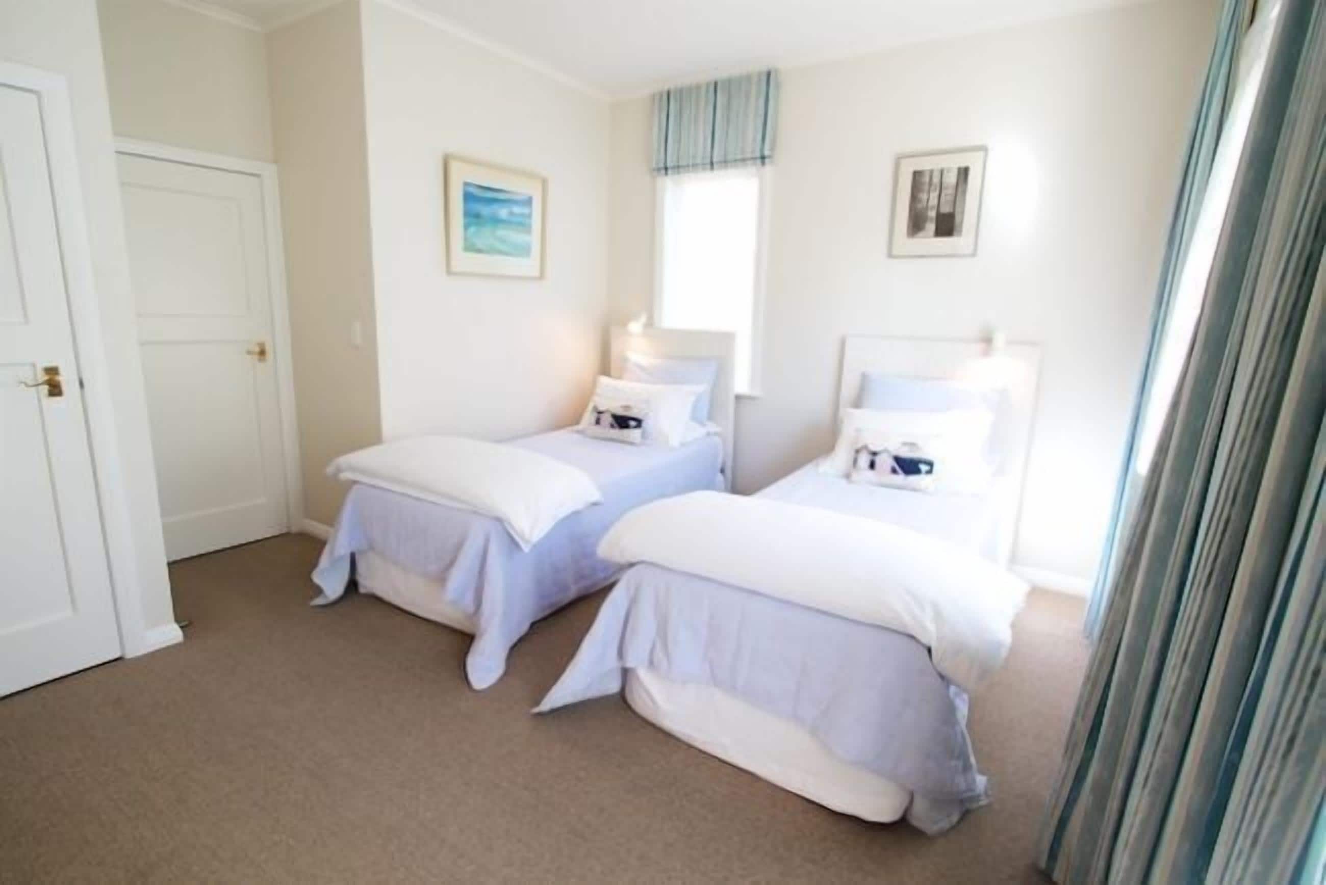 Een slaapkamer met twee bedden, een raam met gordijnen en een deur.