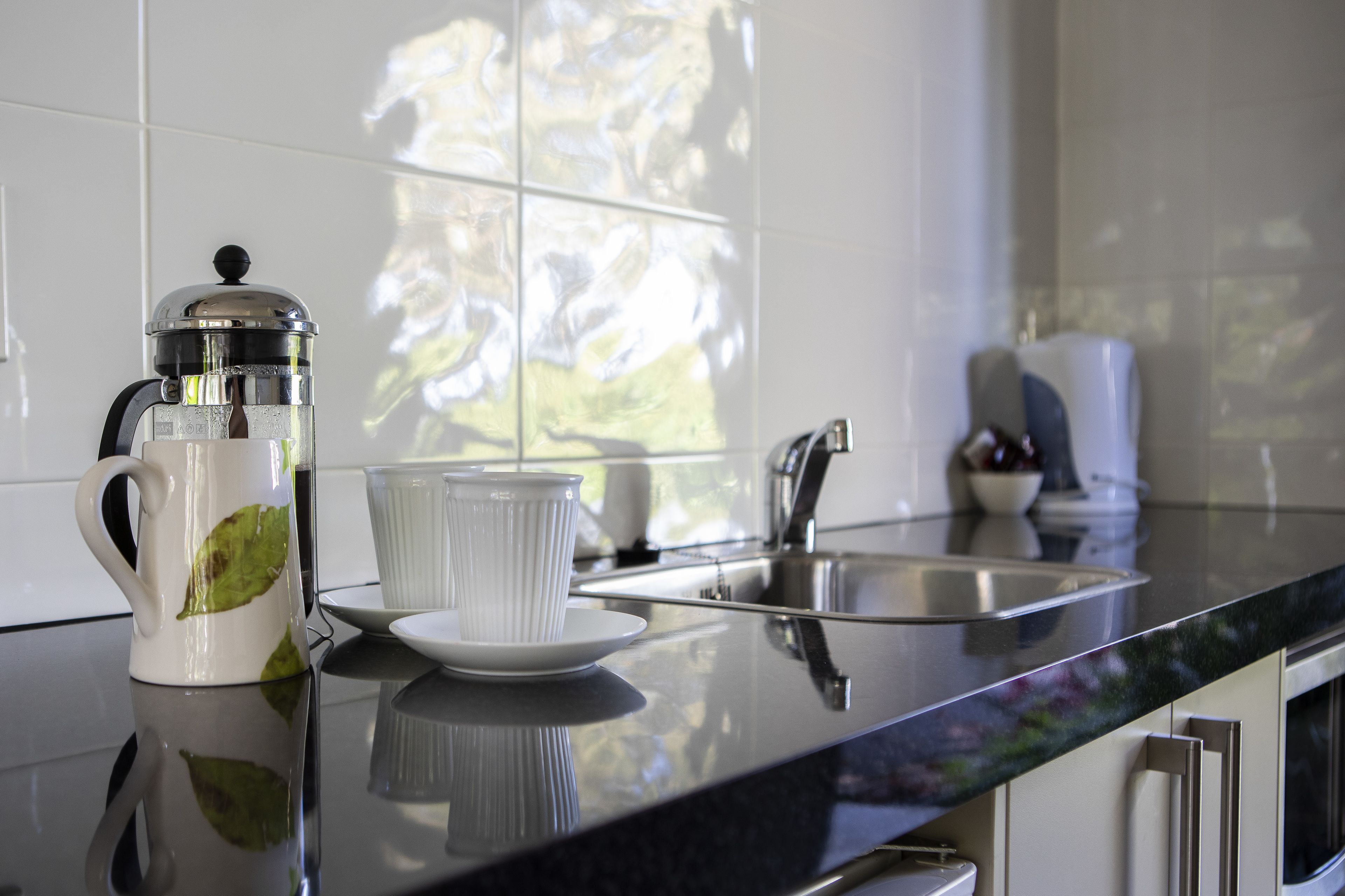 A kitchen with a coffee maker, a cup, and a sink.