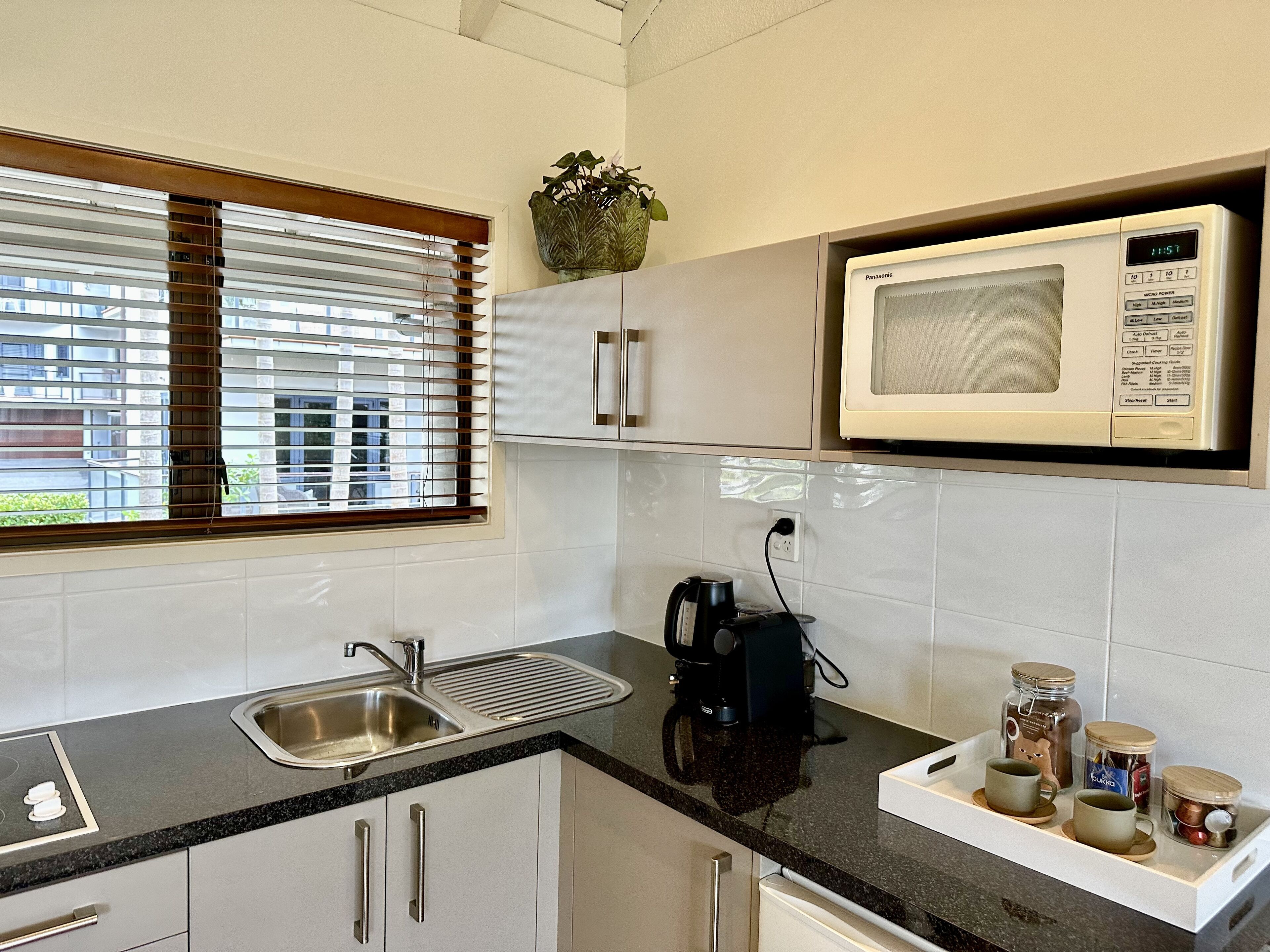 A modern kitchen with a built-in microwave, stainless steel sink, and a window with blinds.