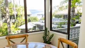 Un comedor con una mesa redonda de vidrio, dos sillas de madera, una pequeña planta en maceta y una revista sobre la mesa.