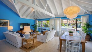 Amplia sala de estar con techo alto, muebles blancos y grandes ventanales que ofrecen vistas al exterior.