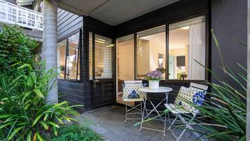 A patio with two white chairs and a table, surrounded by greenery and large windows.