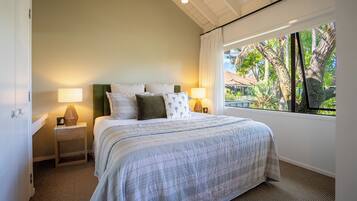 A bedroom with a large bed, two bedside tables with lamps, a view of trees and a house through a window.