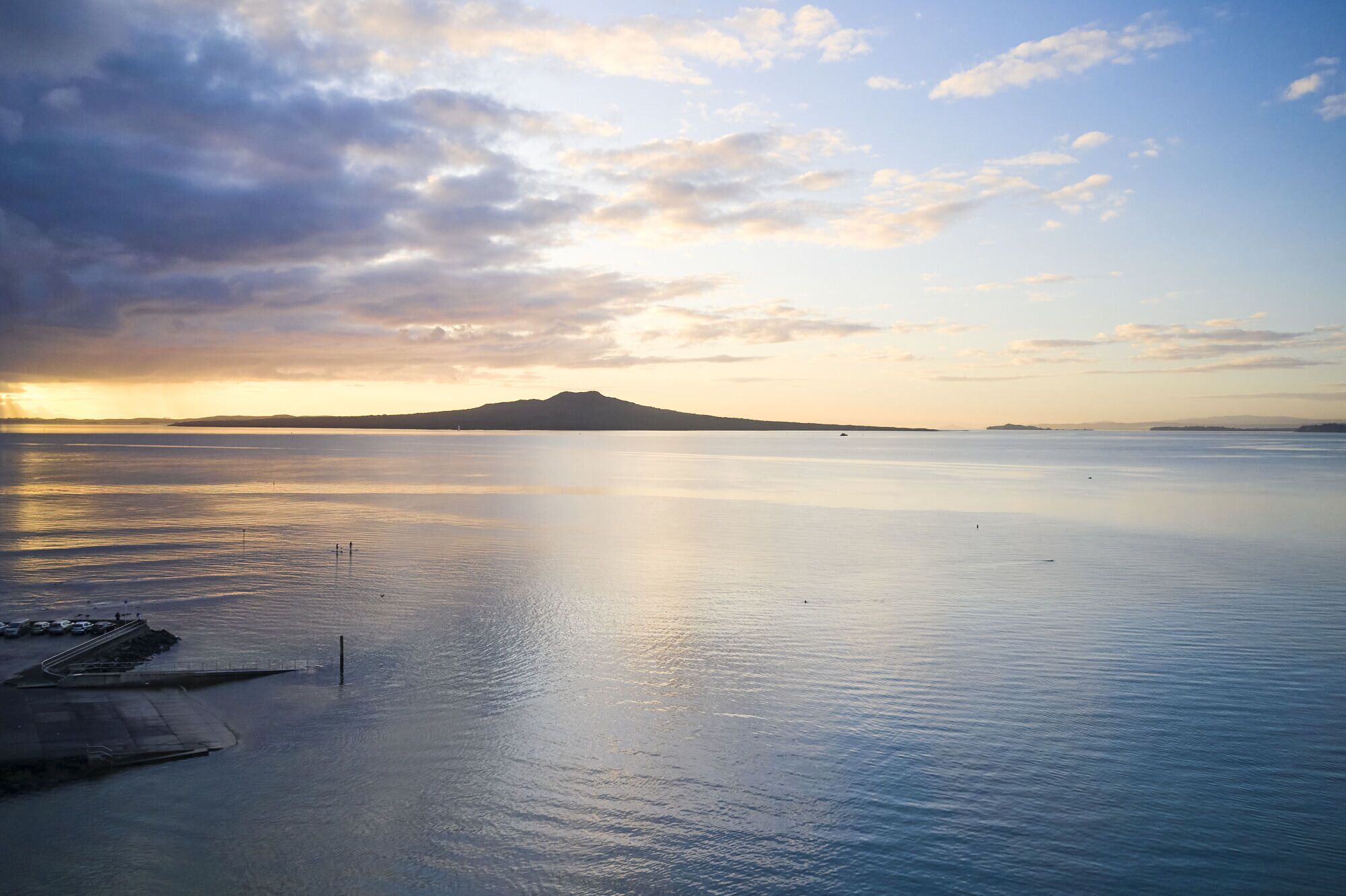 A calm body of water with a dock and a distant mountain.