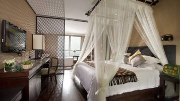 A bedroom with a four-poster bed, a desk with a chair, a television, and a window with a view.