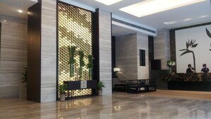 Una hall moderna con reception, area lounge e elementi decorativi come piante e una parete con motivo geometrico.