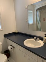 Un baño con un lavamanos blanco, un espejo, un inodoro y un cubo de basura.