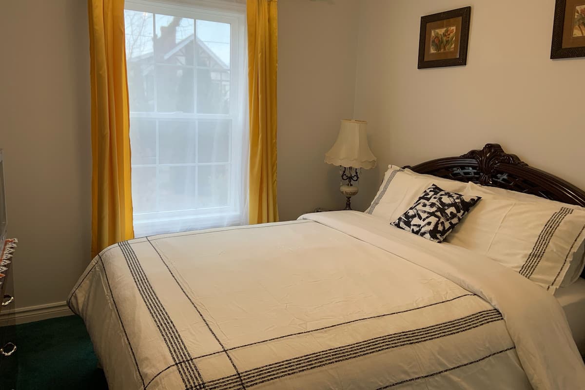 Una cama bien hecha con una colcha de diseño blanco y negro, un cabecero de madera y una única almohada con el mismo estampado.