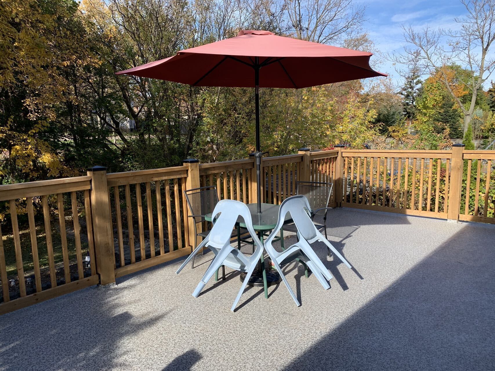 A patio with a table and chairs, a red umbrella, and a wooden fence.