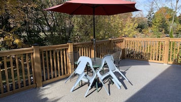 A patio with a table and chairs, a red umbrella, and a wooden fence.