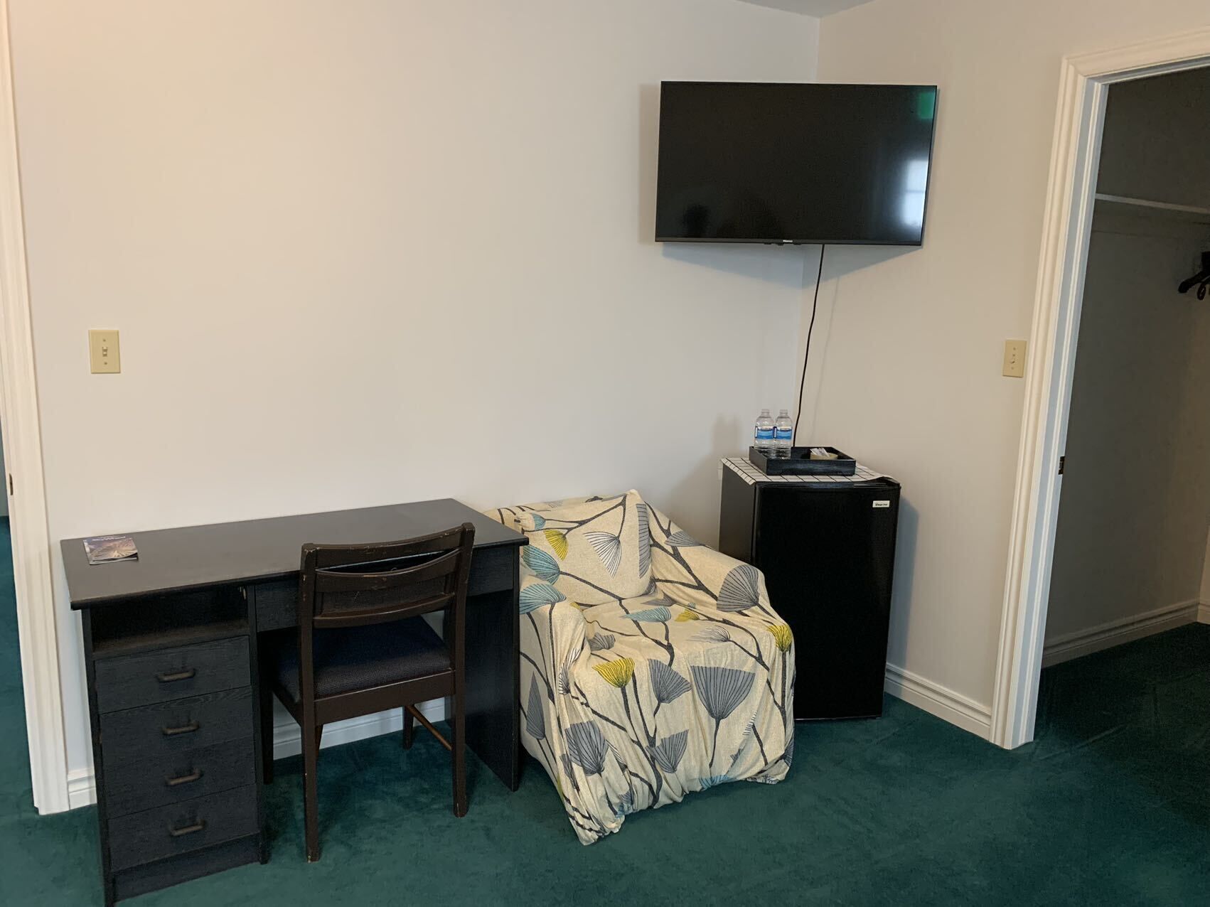 A small room with a desk, chair, and a television mounted on the wall.