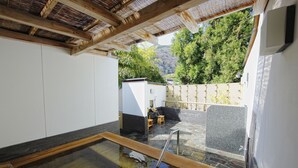 A traditional Japanese onsen with a wooden deck, stone flooring, and a view of a forested hillside. - Arashiyama Benkei (Kyoto)